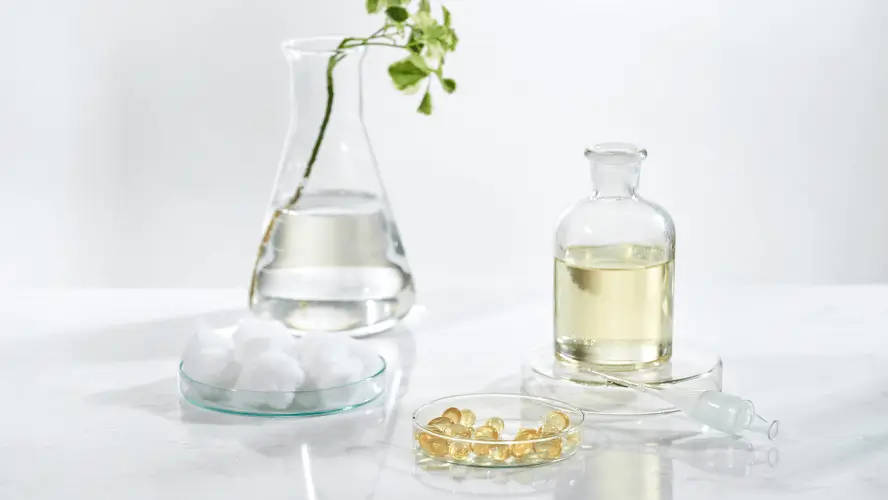 bottle of oil, omega 3 tablets and a lone flower all in arrangement